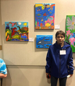 Christian Tresierras standing beside his paintings: "Prehistoric Paradise," "Aqua Adventures," and " Whales."